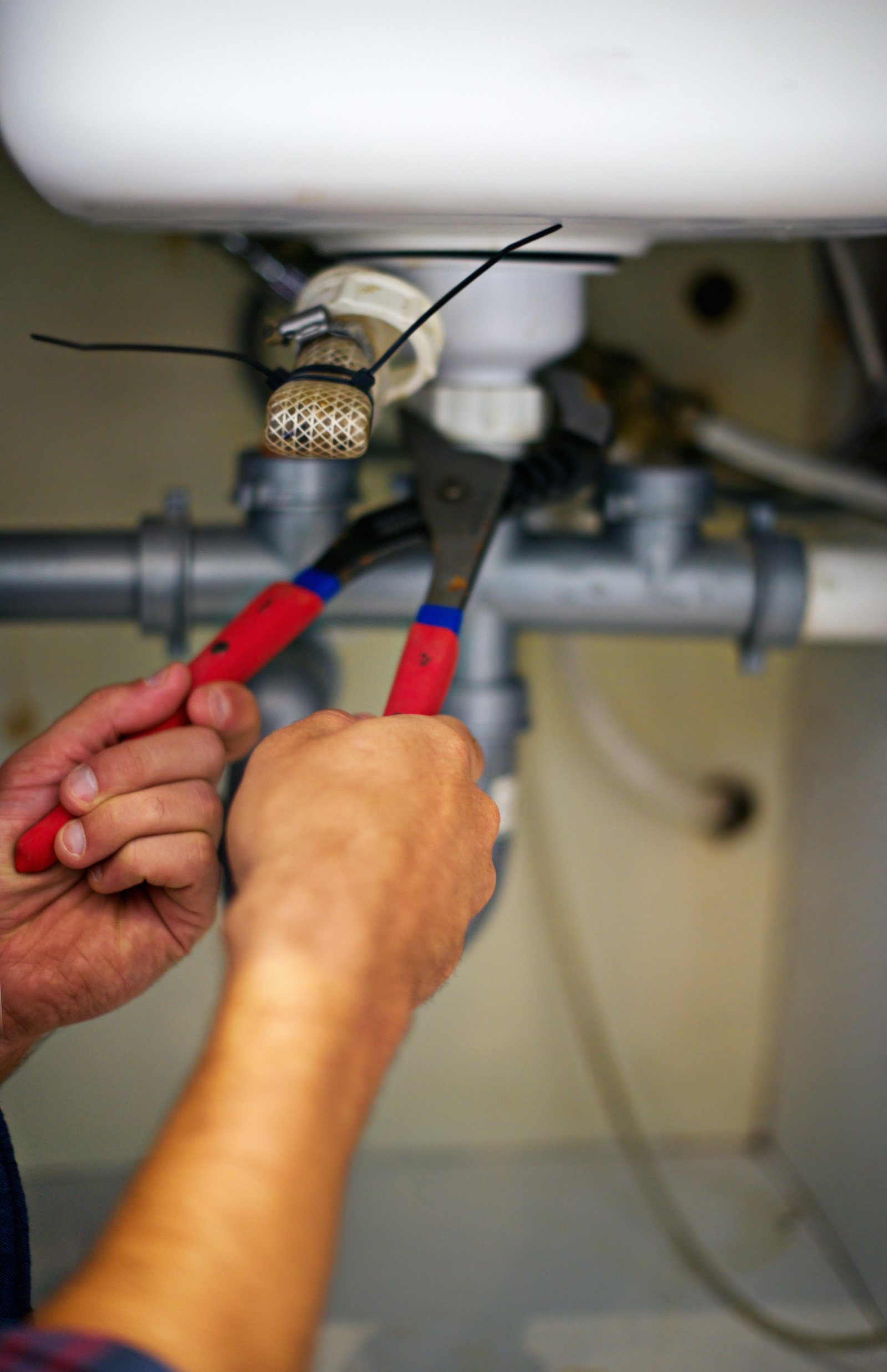 Plumber tightening a drain nut under a sink during a sink repair